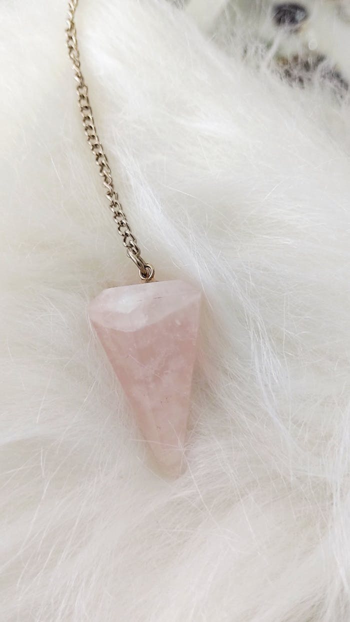 Close-up of a rose quartz gemstone pendant with chain on soft white fur.